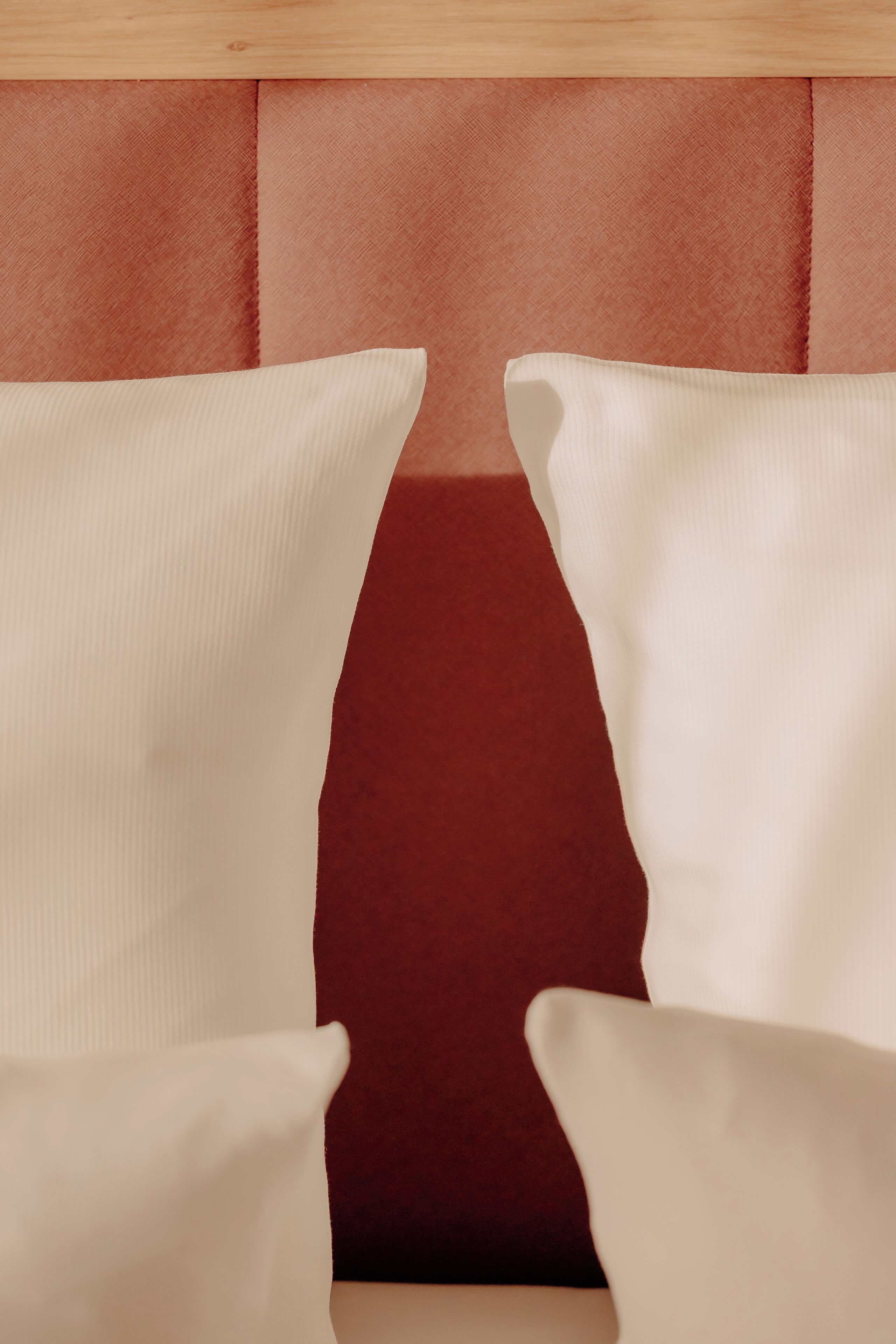 A close-up of a headboard with a red upholstered panel and two white pillows.