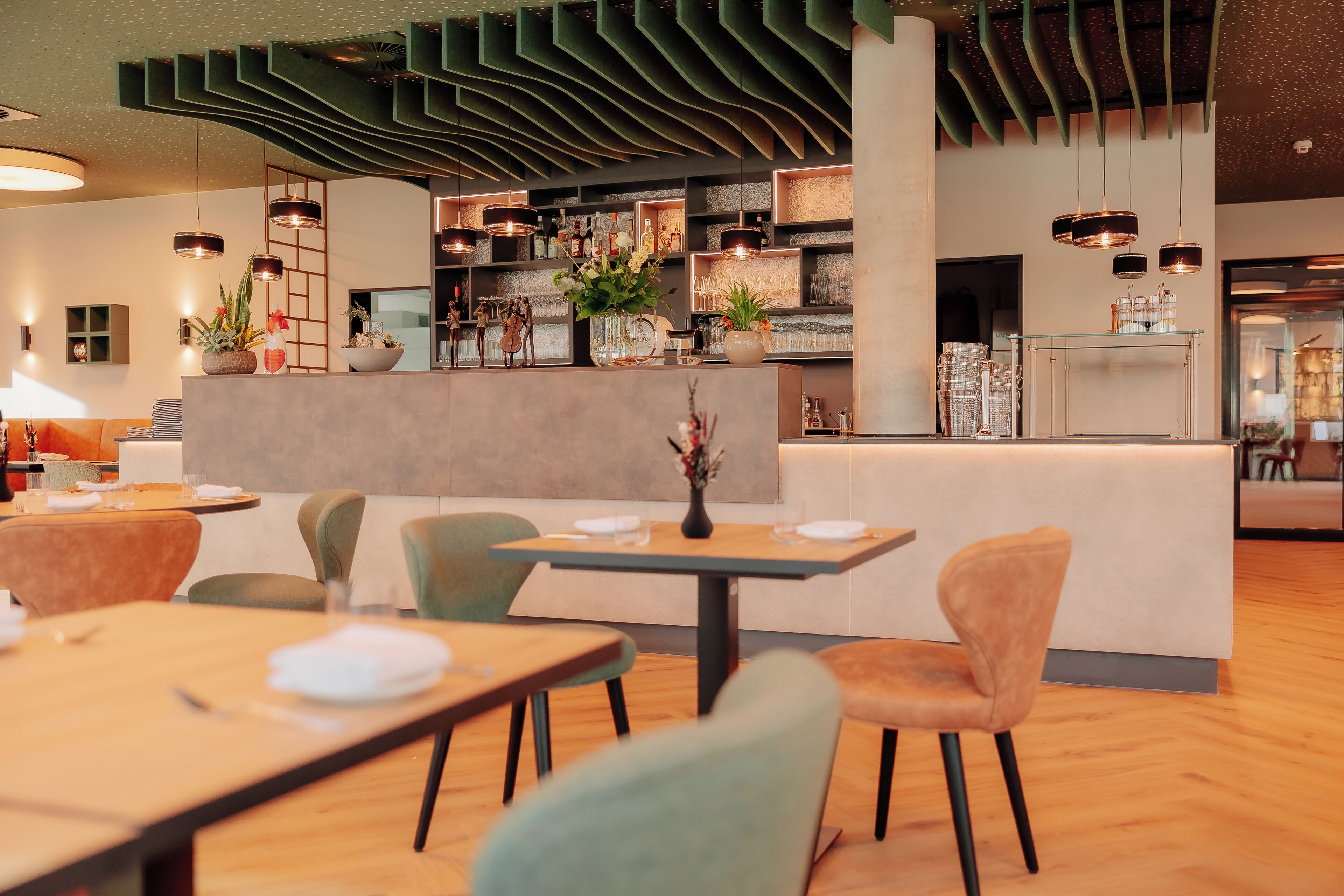 A modern restaurant with a central bar area, multiple seating options, and a variety of plants and decorative items.