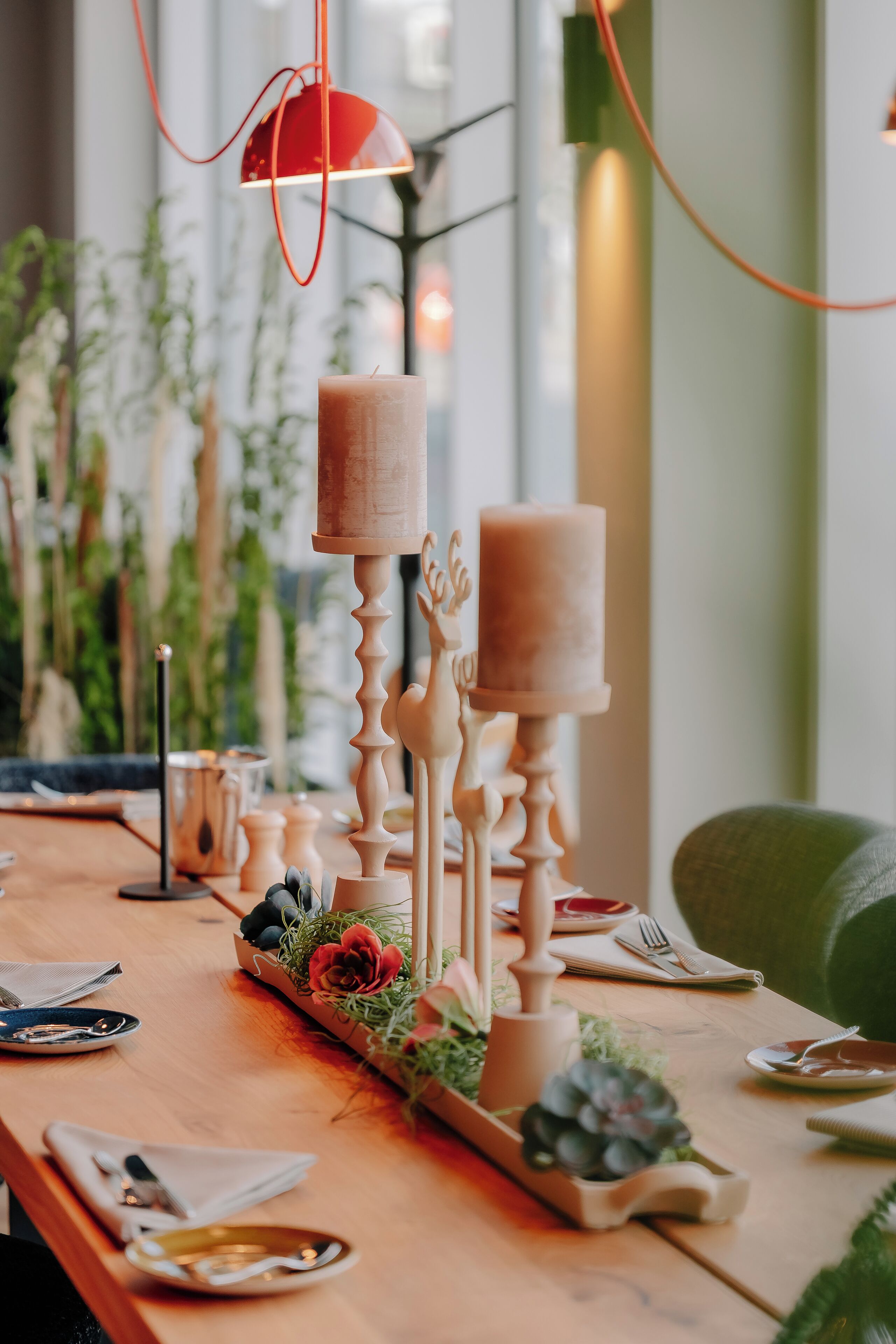 A wooden table set with candles, a red pendant light, and a vase with flowers.