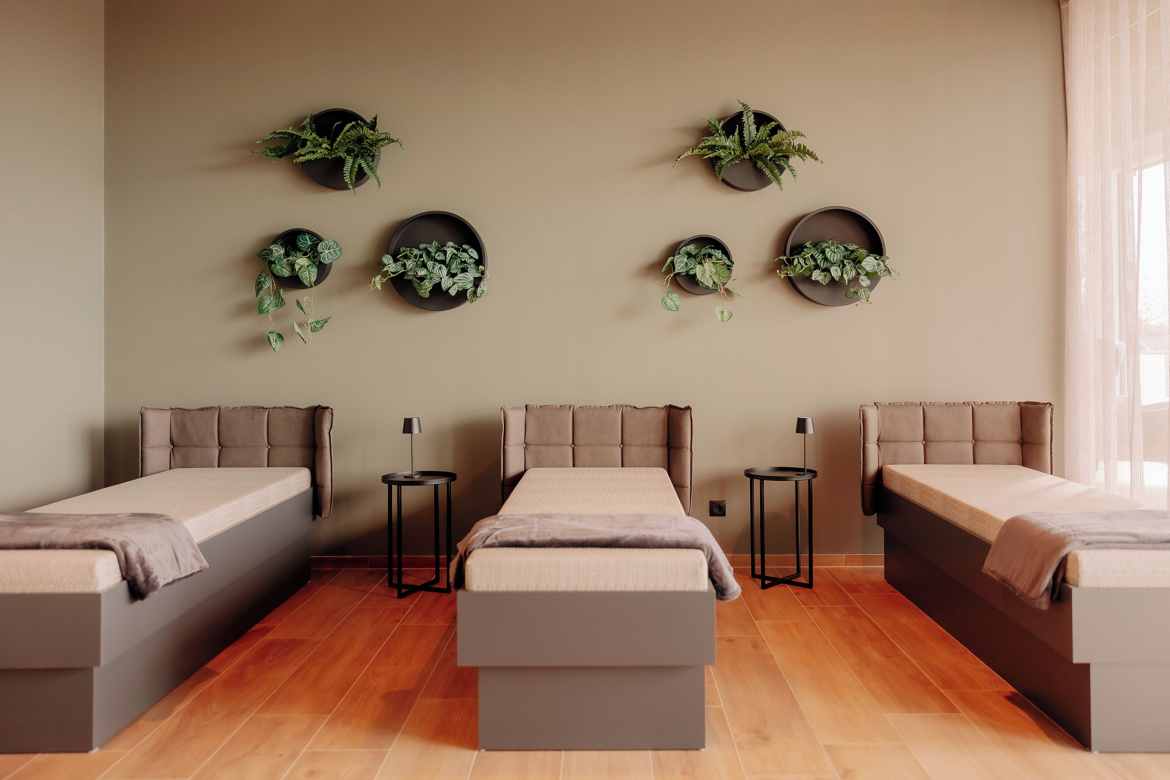 A modern bedroom with three beds, a central bench, and wall-mounted planters.