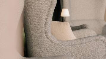 Een grijze bekleden fauteuil met een kussen, geplaatst tegen een muur met een structuur.