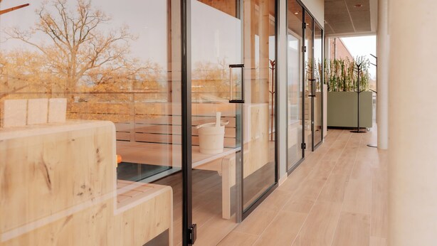 Un interior modern amb separadors de vidre, mobles de fusta i vistes als arbres exteriors.