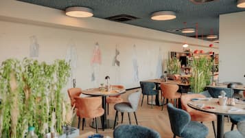 Interior moderno de restaurante con mesas redondas, sillas y un mural en la pared.