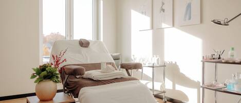 Una habitación moderna con una cama, una mesita con un florero y un carrito con artículos de tocador.