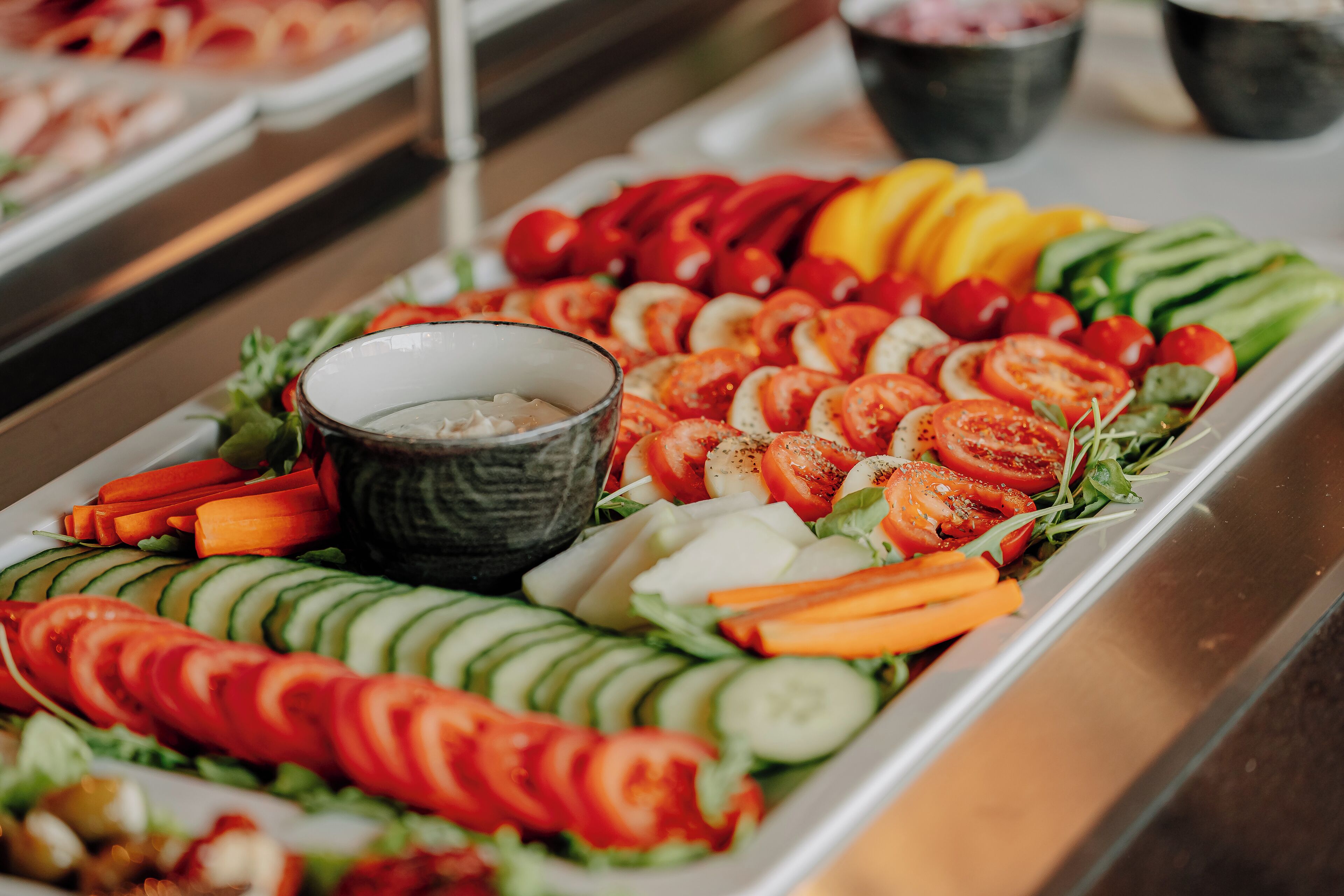 A buffet with various sliced vegetables and a bowl of dip.