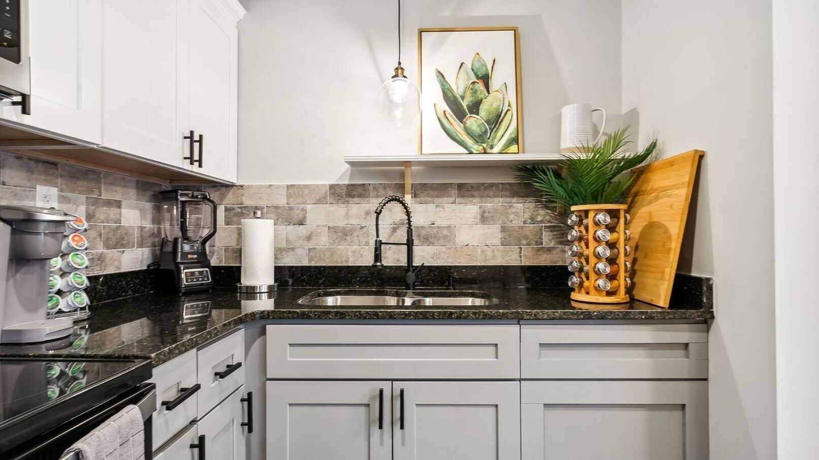 A kitchen with white cabinets, a granite countertop, a stainless steel sink, a coffee maker, and a potted plant.