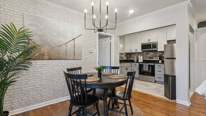 A modern kitchen with white cabinets, stainless steel appliances, and a dining area with a brick wall and a chandelier.