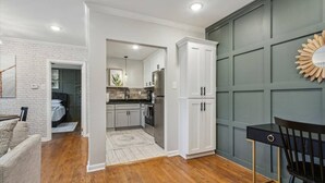 A modern kitchen with white cabinets, a stainless steel refrigerator, and a dining area with a black chair and table.