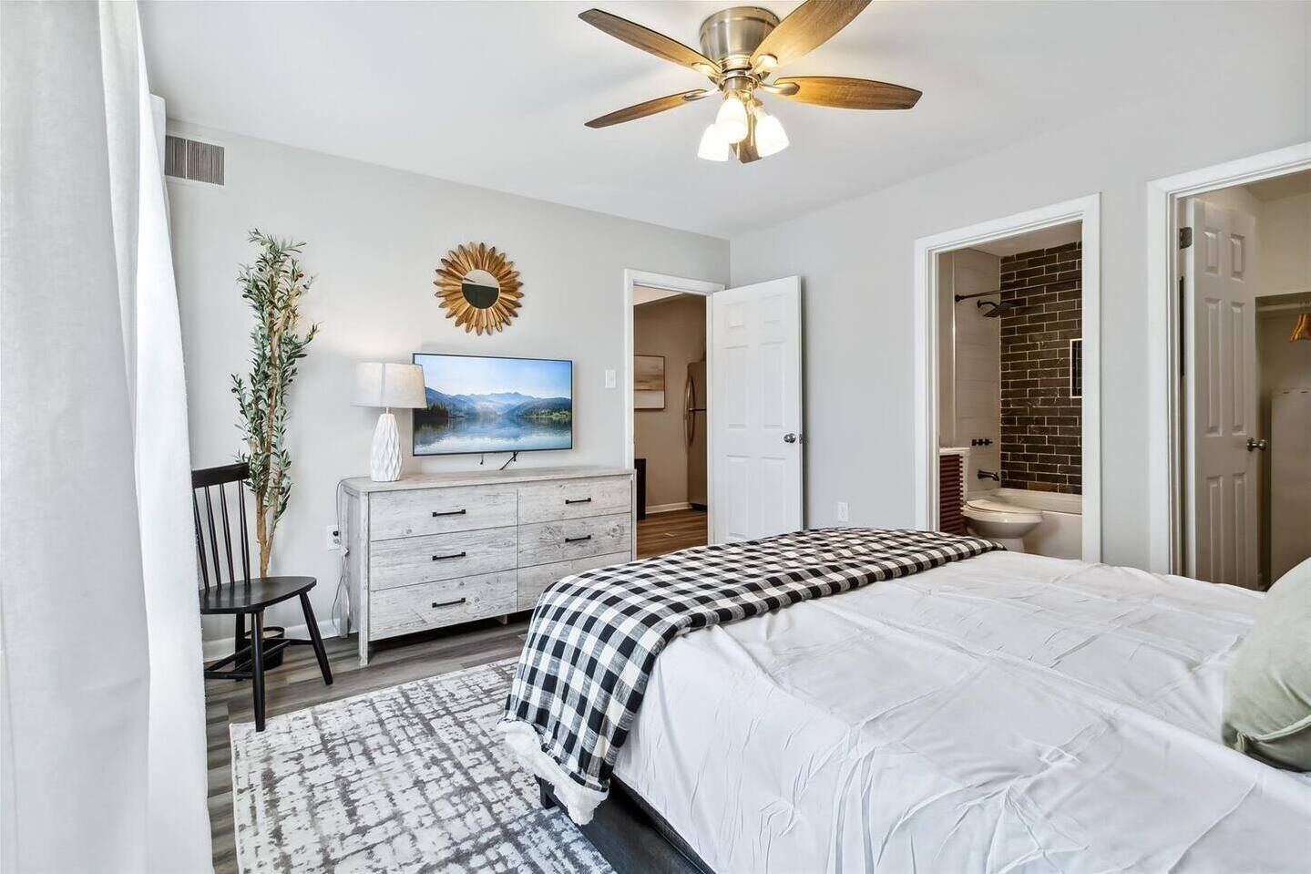 A bedroom with a bed, a dresser, a television, and a ceiling fan.