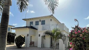 A two-story building with a patio area, palm trees, and a garden with pink flowers. - Villa 1A Relax & Dive Resort Bonaire Village (Kralendijk)