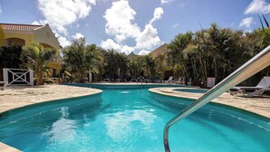 A swimming pool with lounge chairs, palm trees, and a building with a tiled roof. - Villa 1A Relax & Dive Resort Bonaire Village (Kralendijk)