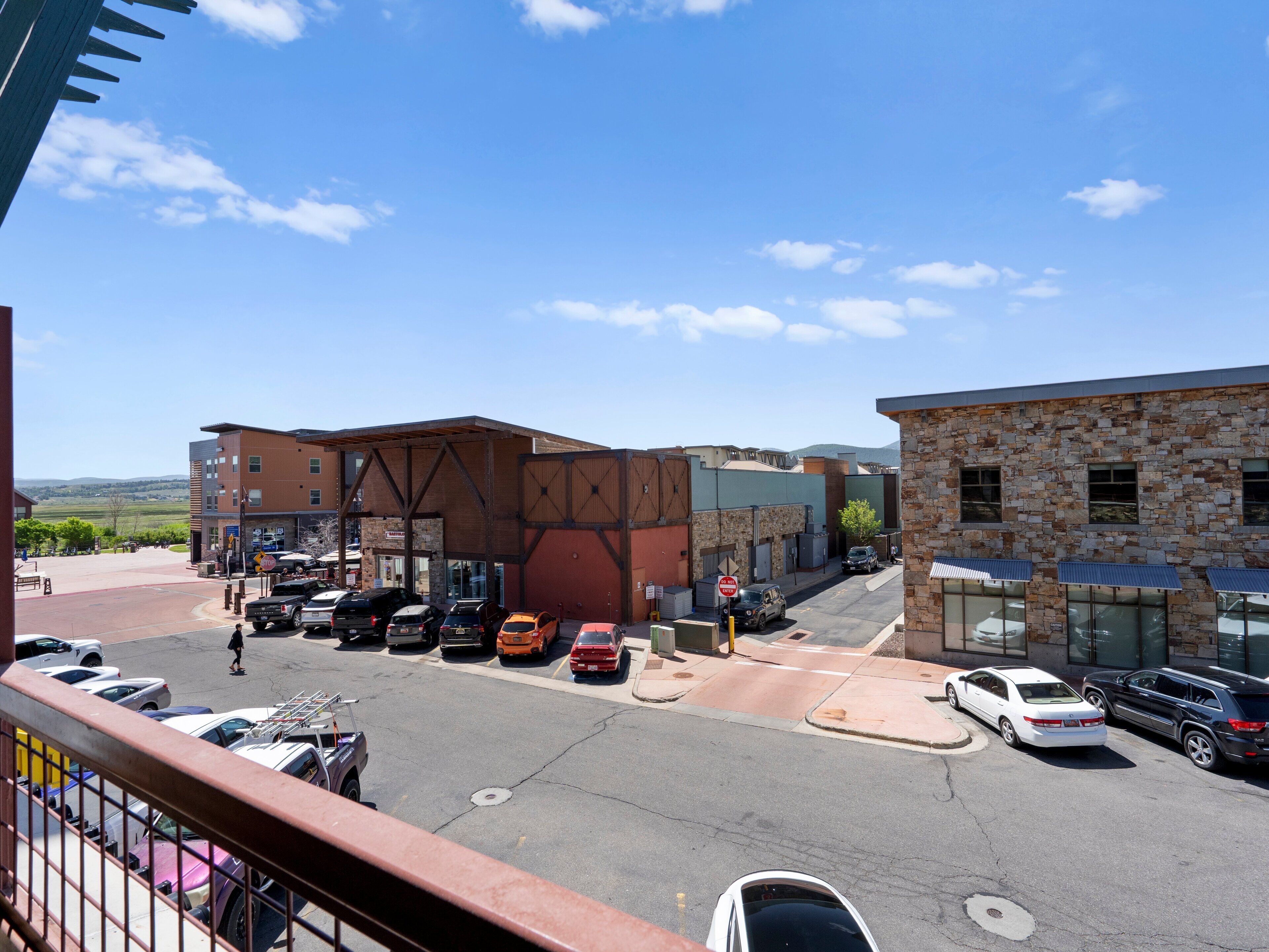 A parking lot with several cars, a pedestrian crossing, and buildings with a mix of brick and stone facades.