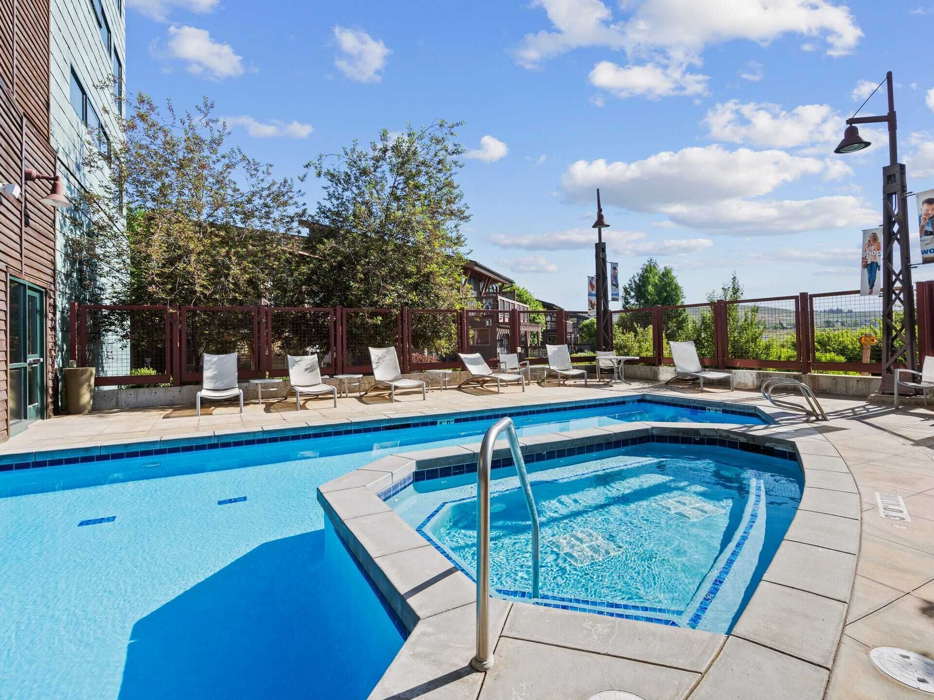 A swimming pool with lounge chairs, a pergola, and a view of the surrounding landscape.