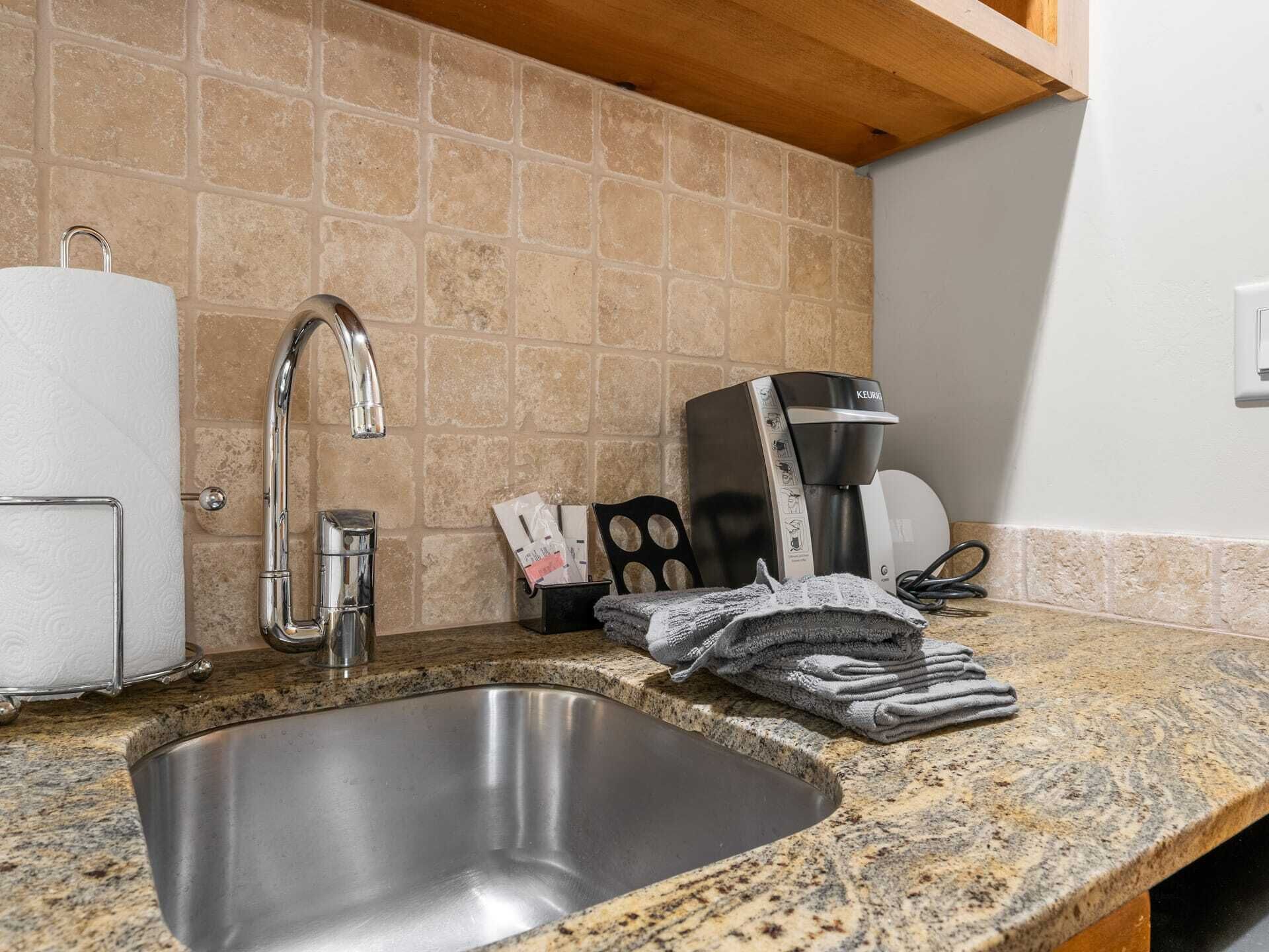 A kitchen with a granite countertop, stainless steel sink, and a coffee maker.