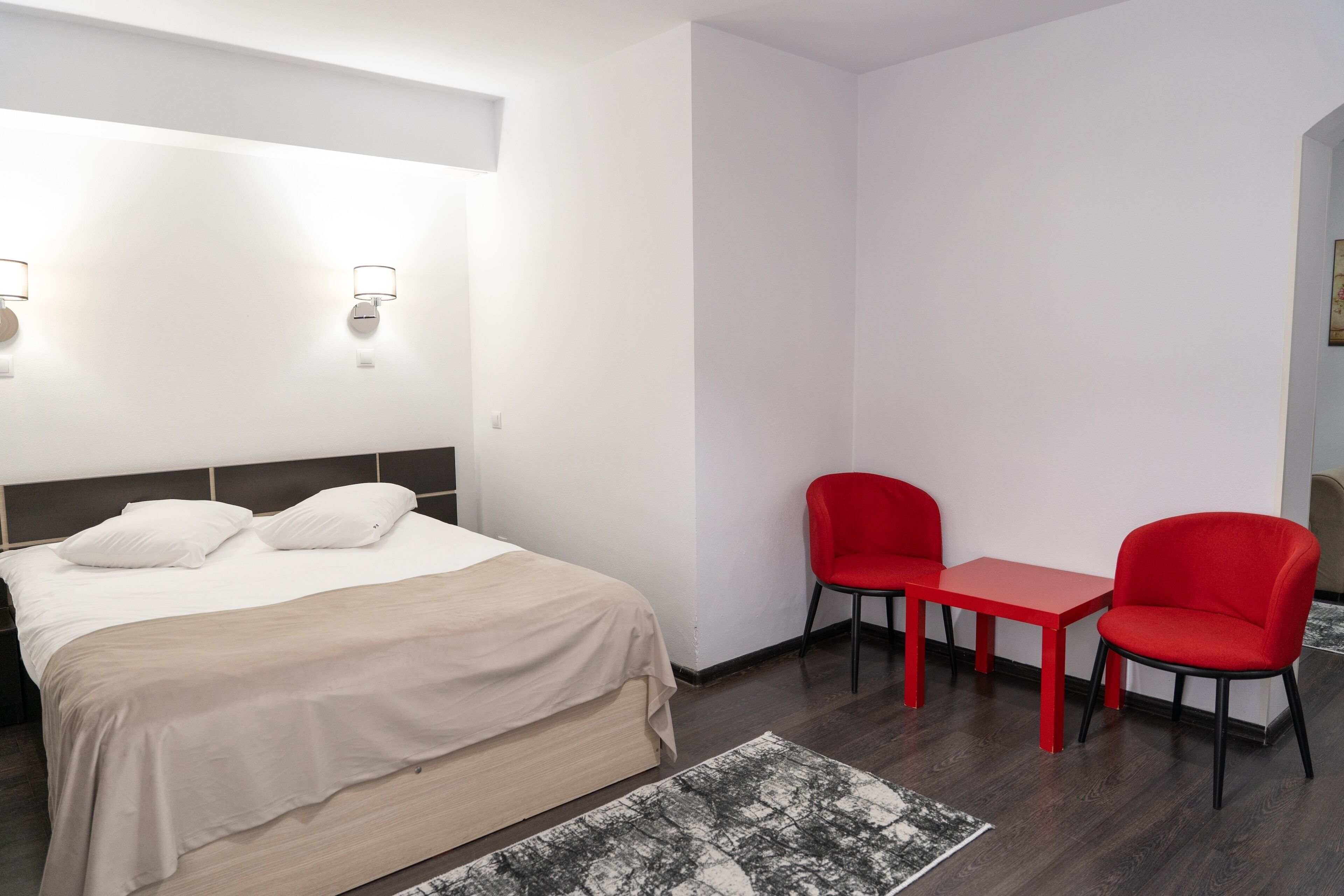 Une chambre d’hôtel avec un lit, deux chaises rouges, une petite table et une table de chevet.