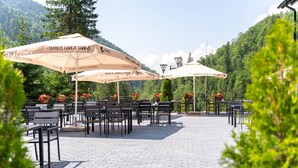 An outdoor seating area with tables and chairs, surrounded by greenery and a mountainous backdrop.