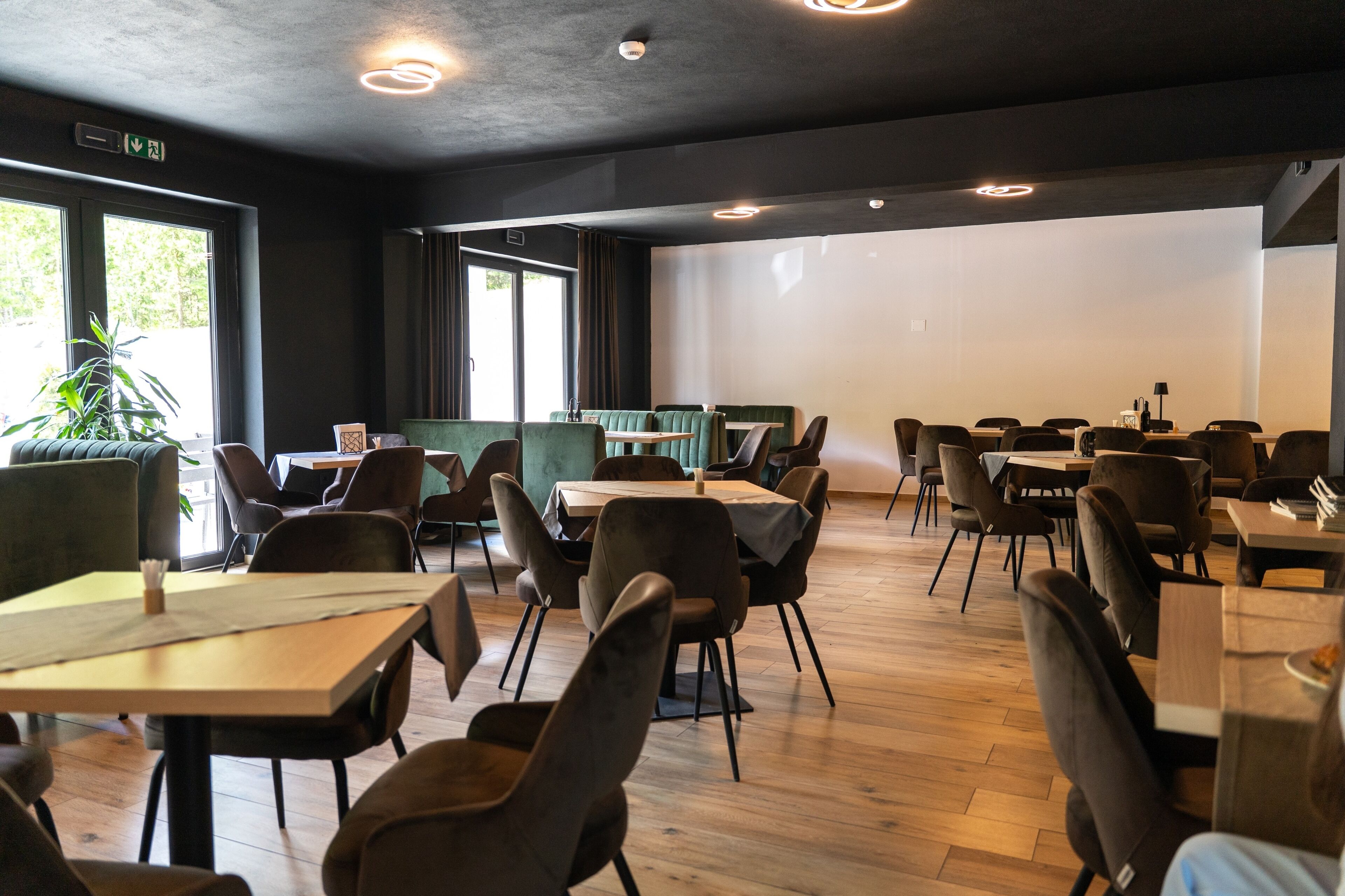 Un restaurante con mesas, sillas, una planta y un ventanal grande.