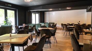 Un restaurante con mesas, sillas, una planta y un ventanal grande.
