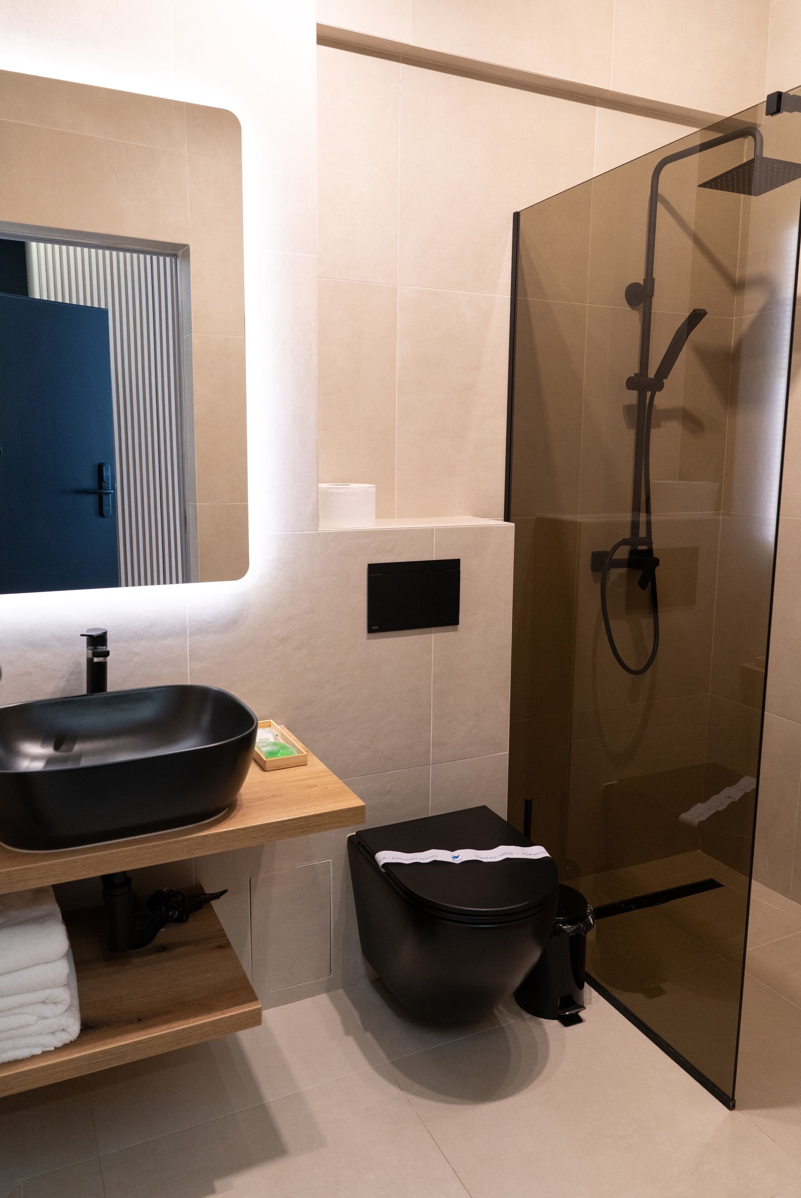 Un baño moderno con ducha envuelta en vidrio, un lavabo negro y un tocador de madera.