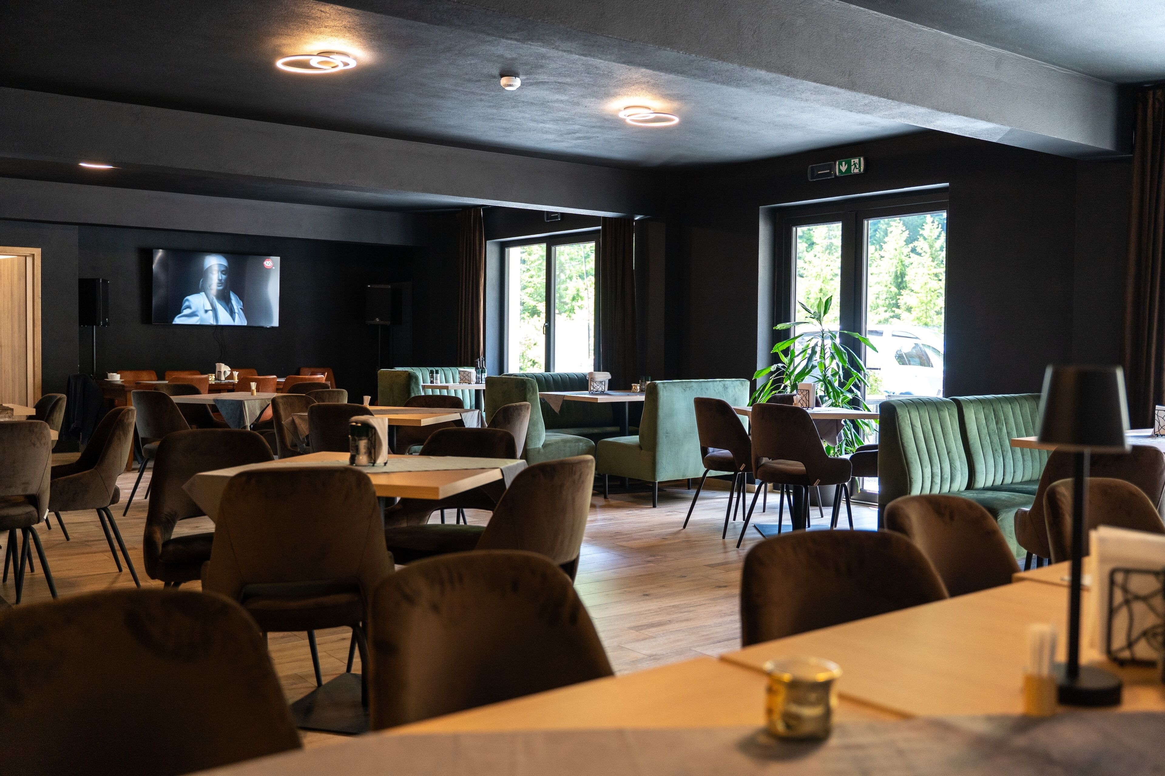 A modern restaurant with a flat-screen TV, multiple seating areas, and large windows.