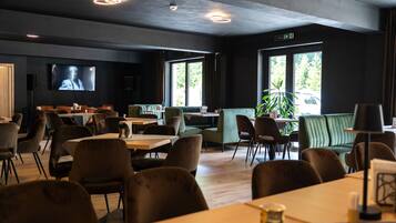 A modern restaurant with a flat-screen TV, multiple seating areas, and large windows.