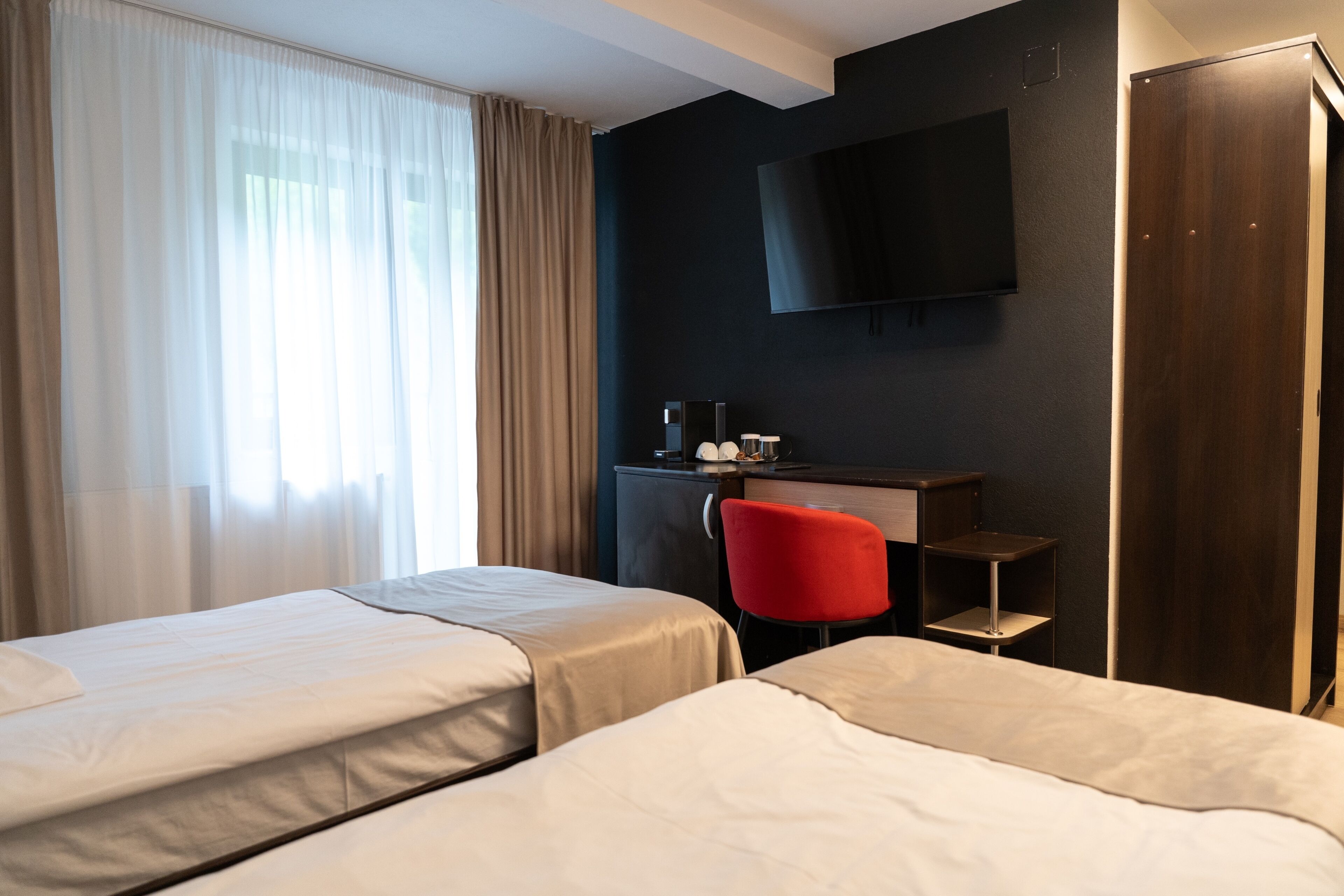 A hotel room with two beds, a desk with a chair, a TV mounted on the wall, and a wardrobe.
