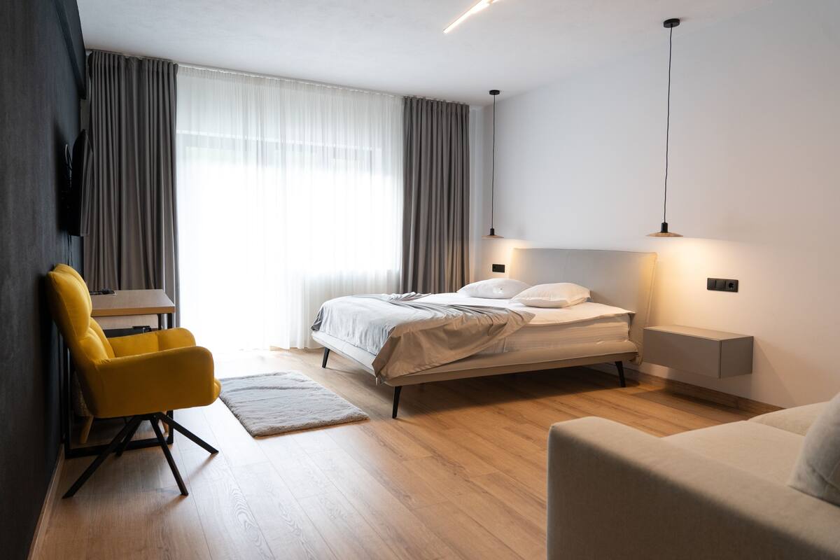 A modern hotel room with a bed, a sofa, a chair, a desk, and a TV.