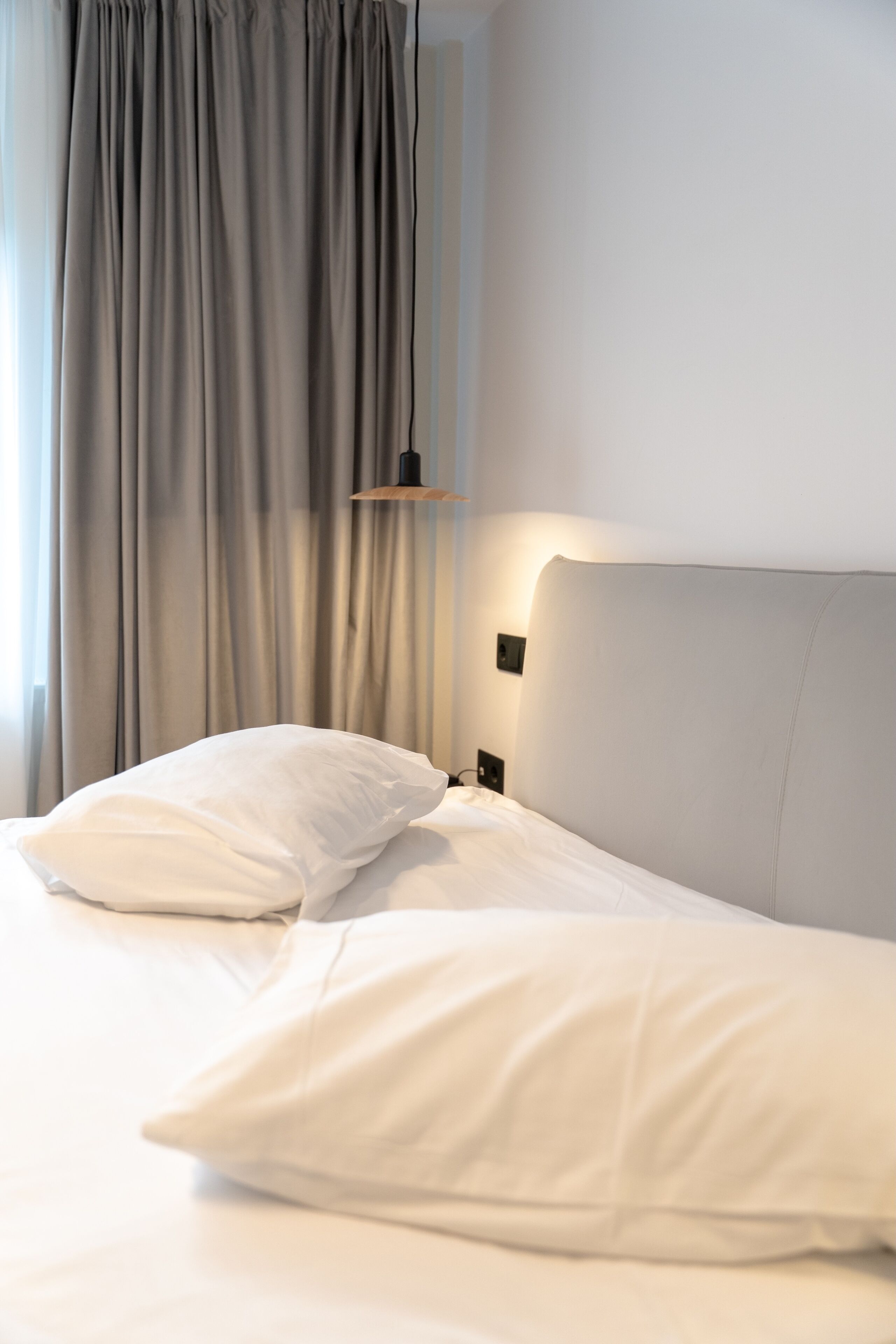 A neatly made bed with pillows, a bedside lamp, and a window with curtains.