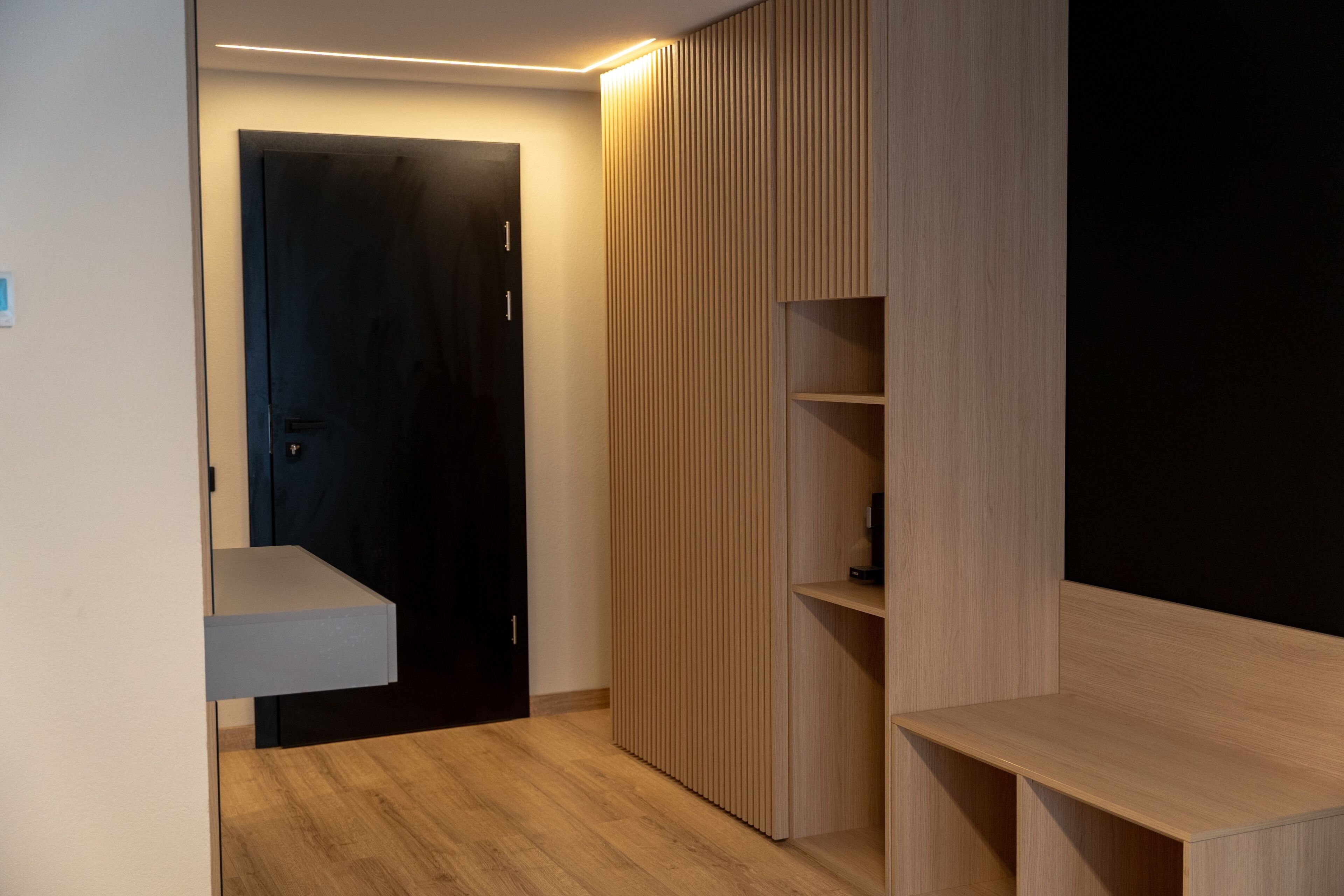 A modern room with a dark door, wooden paneling, and built-in shelving.