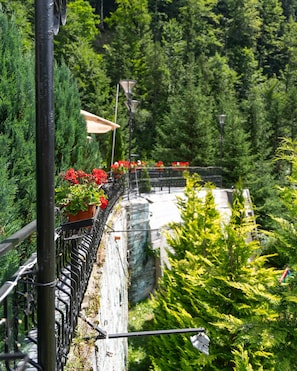 Un espacio al aire libre con vistas panorámicas, barandilla de metal, plantas en macetas y un muro de piedra.