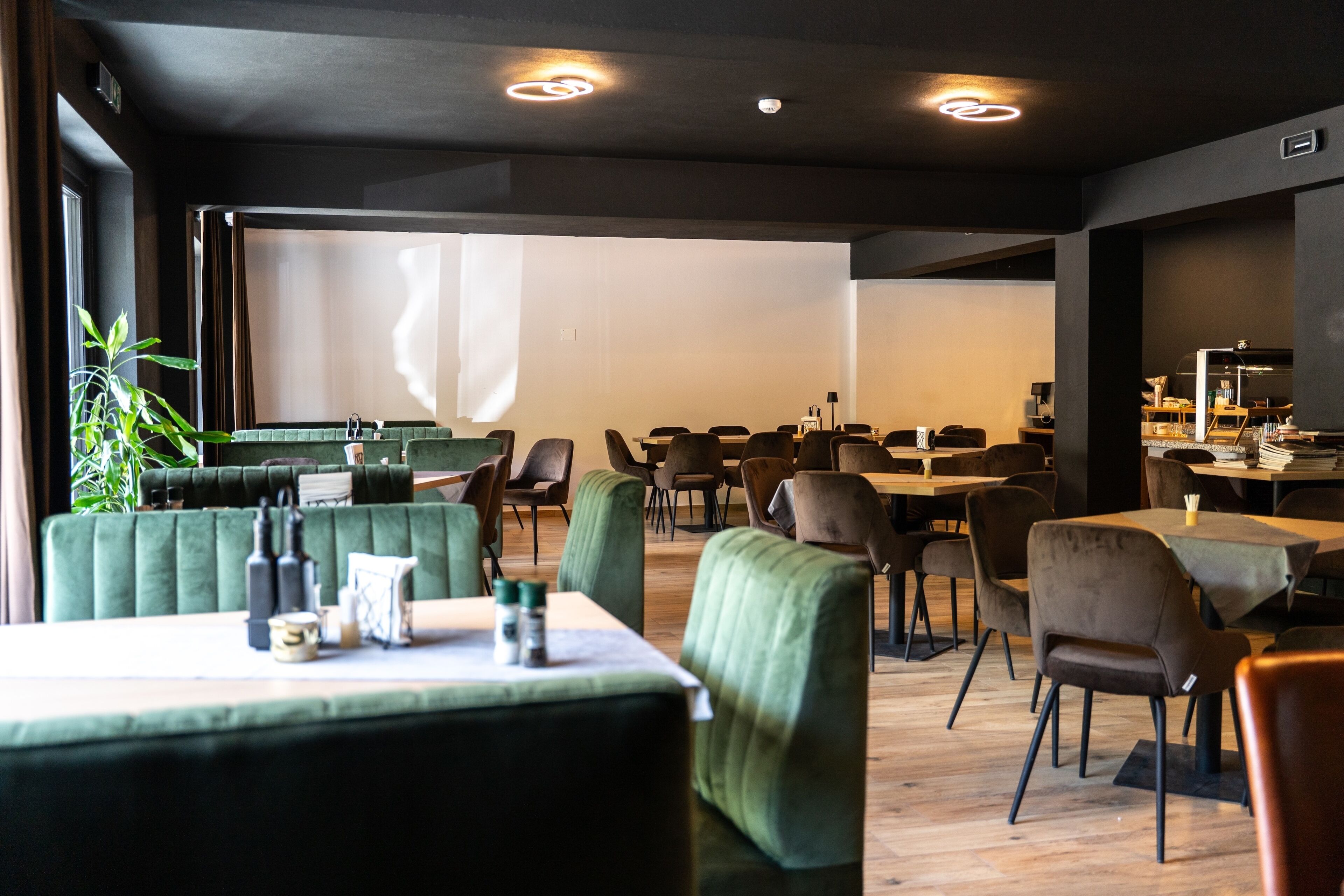 Un restaurante moderno con asientos tapizados en verde, mesas de madera y un amplio ventanal con cortinas.
