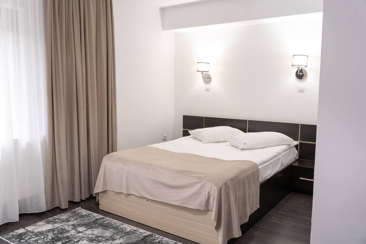 A modern hotel room with a bed, bedside tables, and a nightstand.