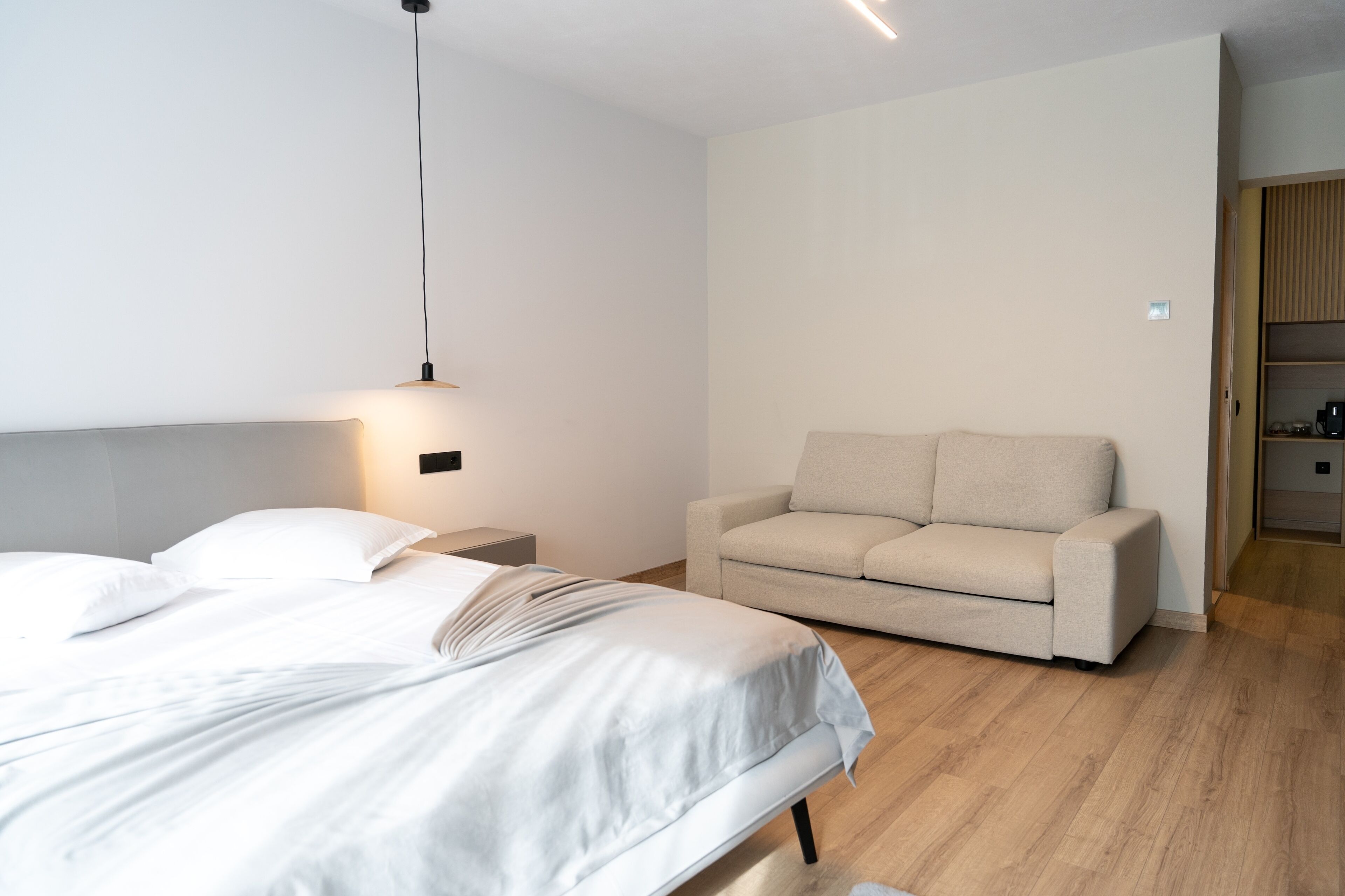 A modern hotel room with a bed, a sofa, and a nightstand.