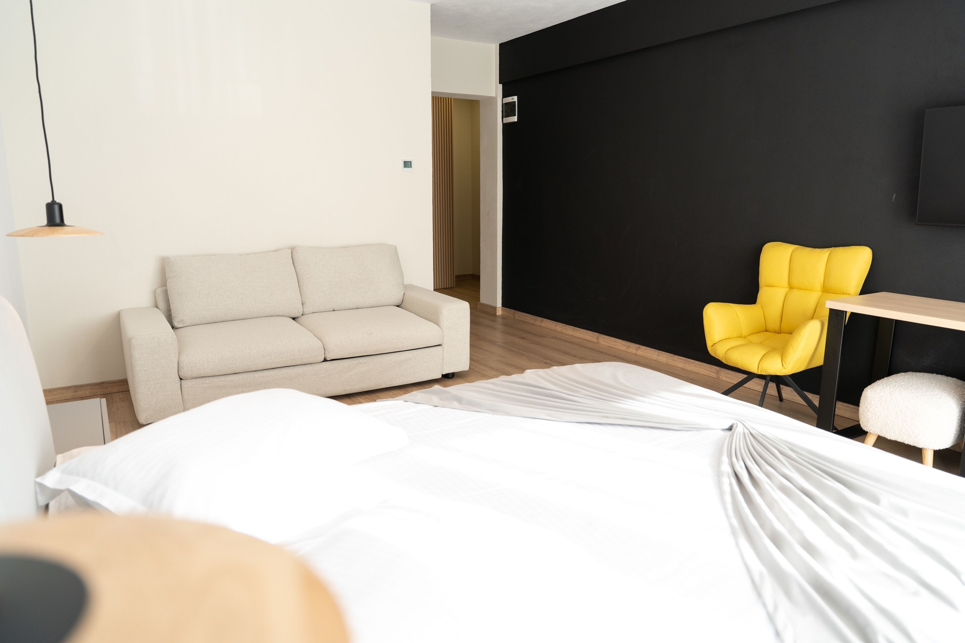Habitació d'hotel moderna amb un llit, un sofà, una cadira groga, una taula petita i un televisor fixat a la paret.