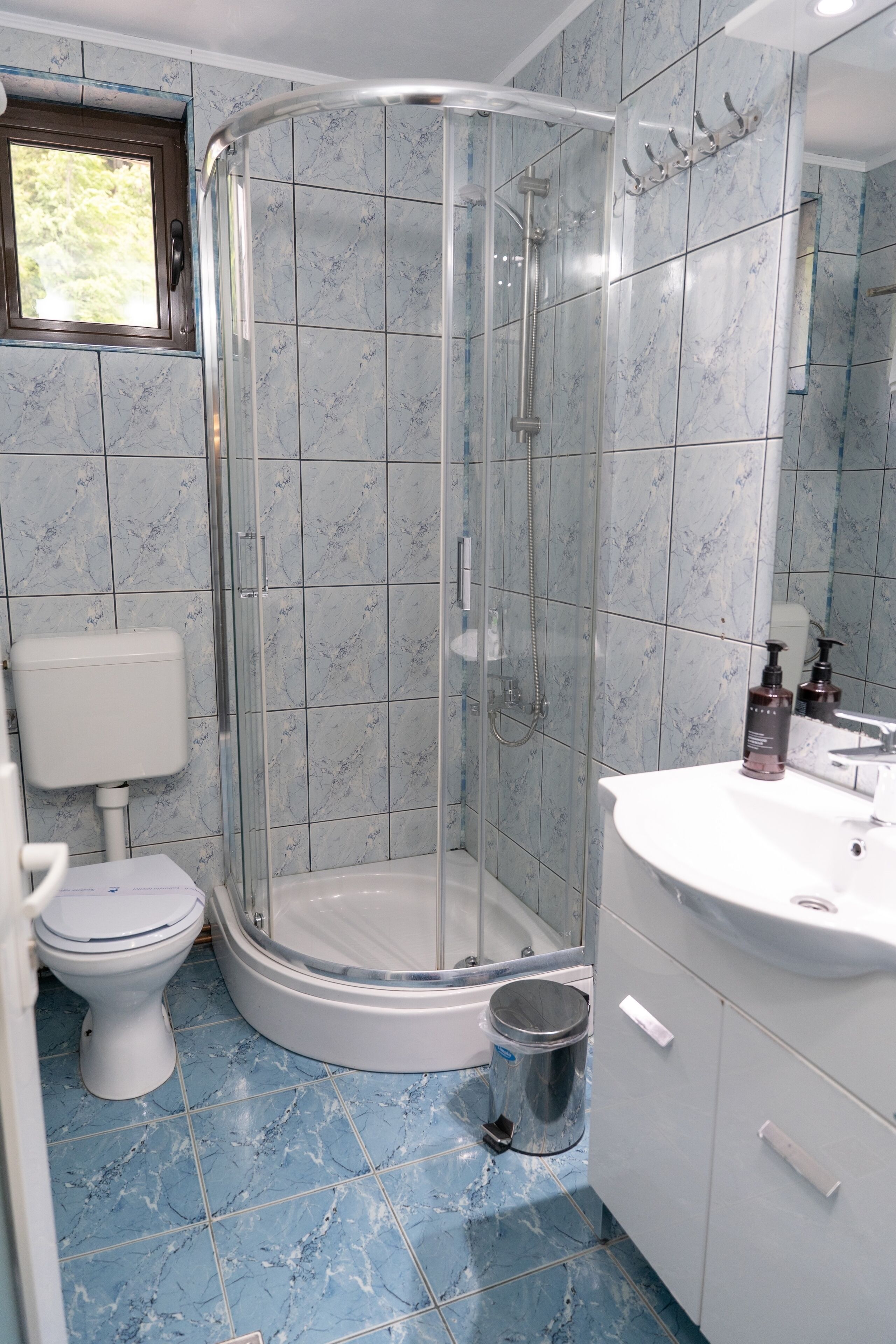 A bathroom with a glass-enclosed shower, a toilet, a sink with a mirror, and a window.