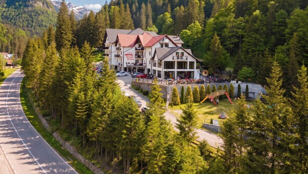A hotel with a red roof, multiple balconies, and a view of a forested mountain.