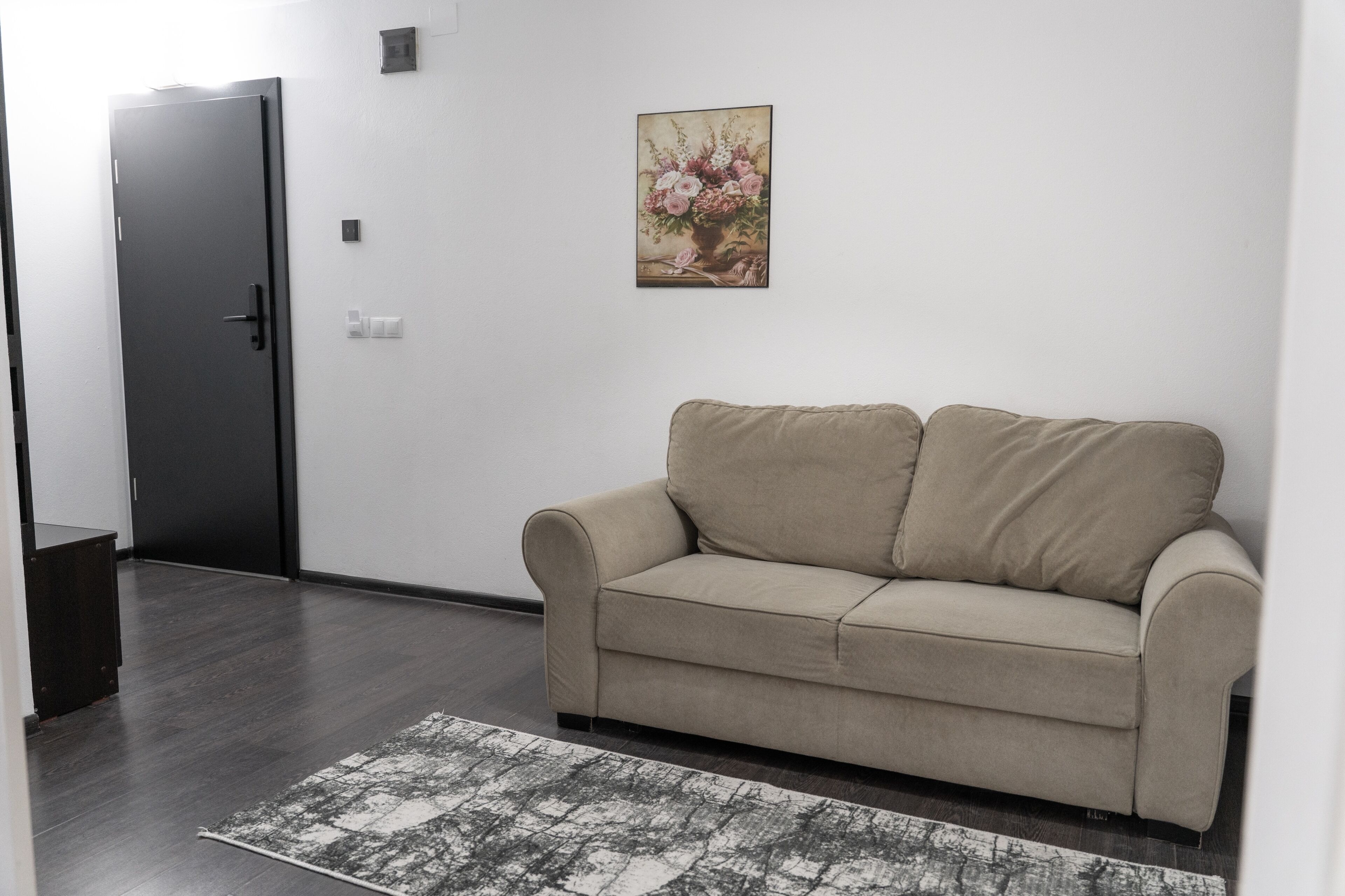 A neutral-toned room with a beige sofa, a patterned rug, a door, and a framed floral artwork on the wall.