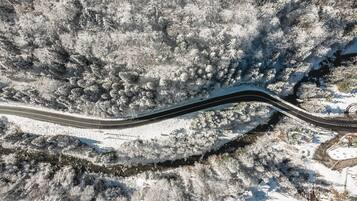 Vista aérea de un camino sinuoso que atraviesa un paisaje nevado con árboles densos cubiertos de escarcha.