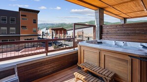 Una terraza de madera con un jacuzzi y escalones que conducen a un balcón con vistas a un pueblo.