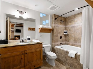 A modern bathroom with a wooden vanity, a toilet, a bathtub, and a shower area with tiled walls. - Newpark 216 | Private Hot Tub | Kitchenette | Fireplace | Washer/Dryer | Mtn & Preserve Views | Pool (Park City)