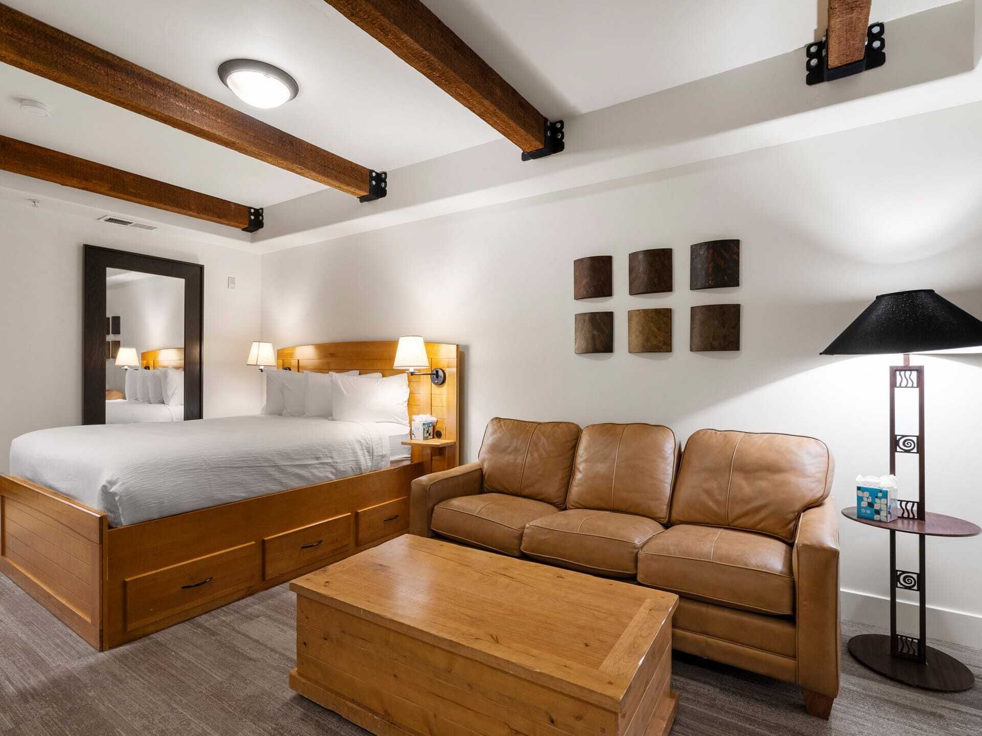Une chambre d’hôtel avec un grand lit, une table basse en bois, un canapé en cuir et une petite table d’appoint.