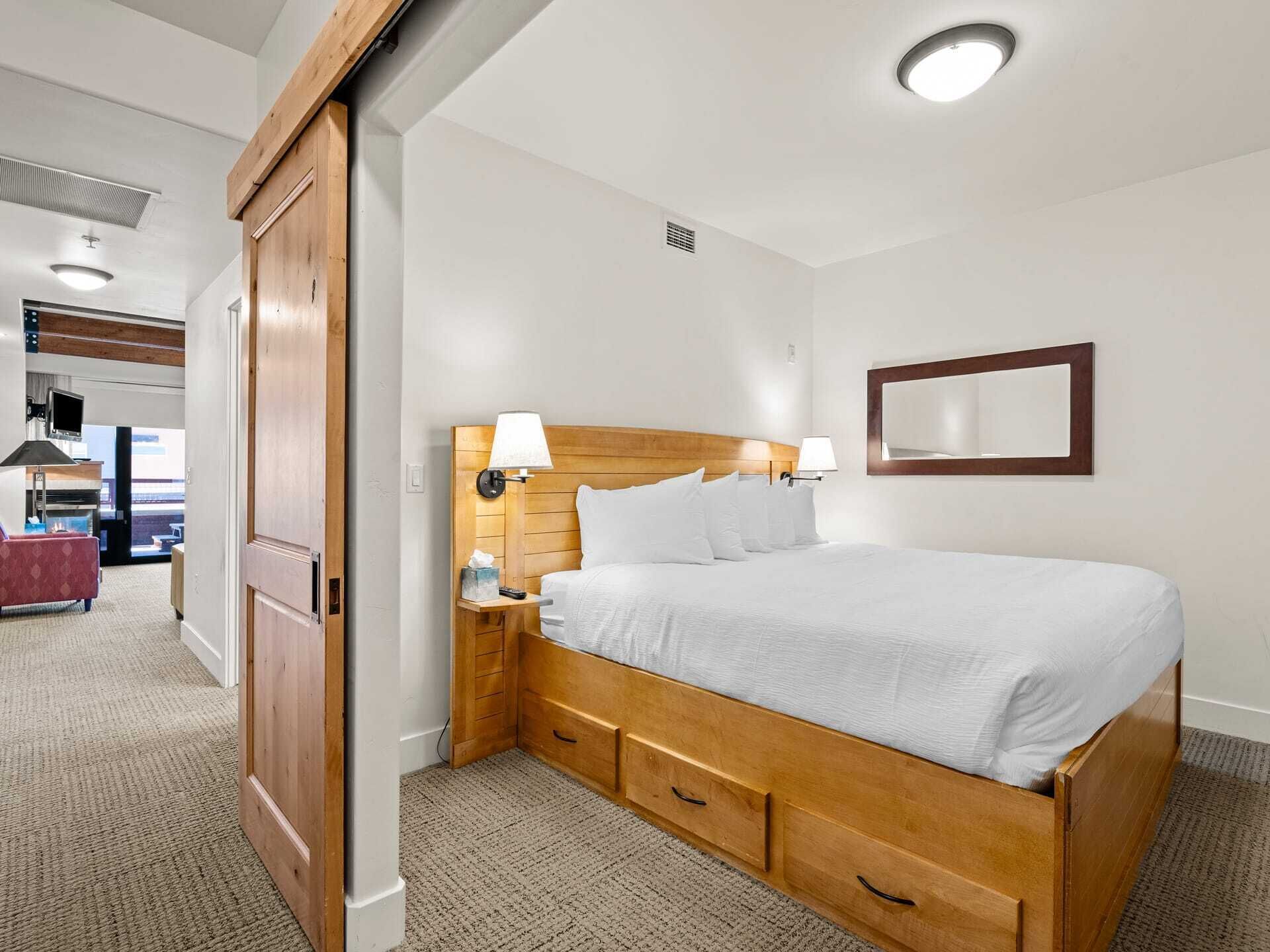 Une chambre d’hôtel avec un lit en bois, des lampes de chevet, un téléviseur à écran plat et un grand miroir au mur.