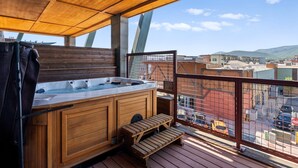 A wooden deck with a hot tub, wooden benches, and a view of the city.