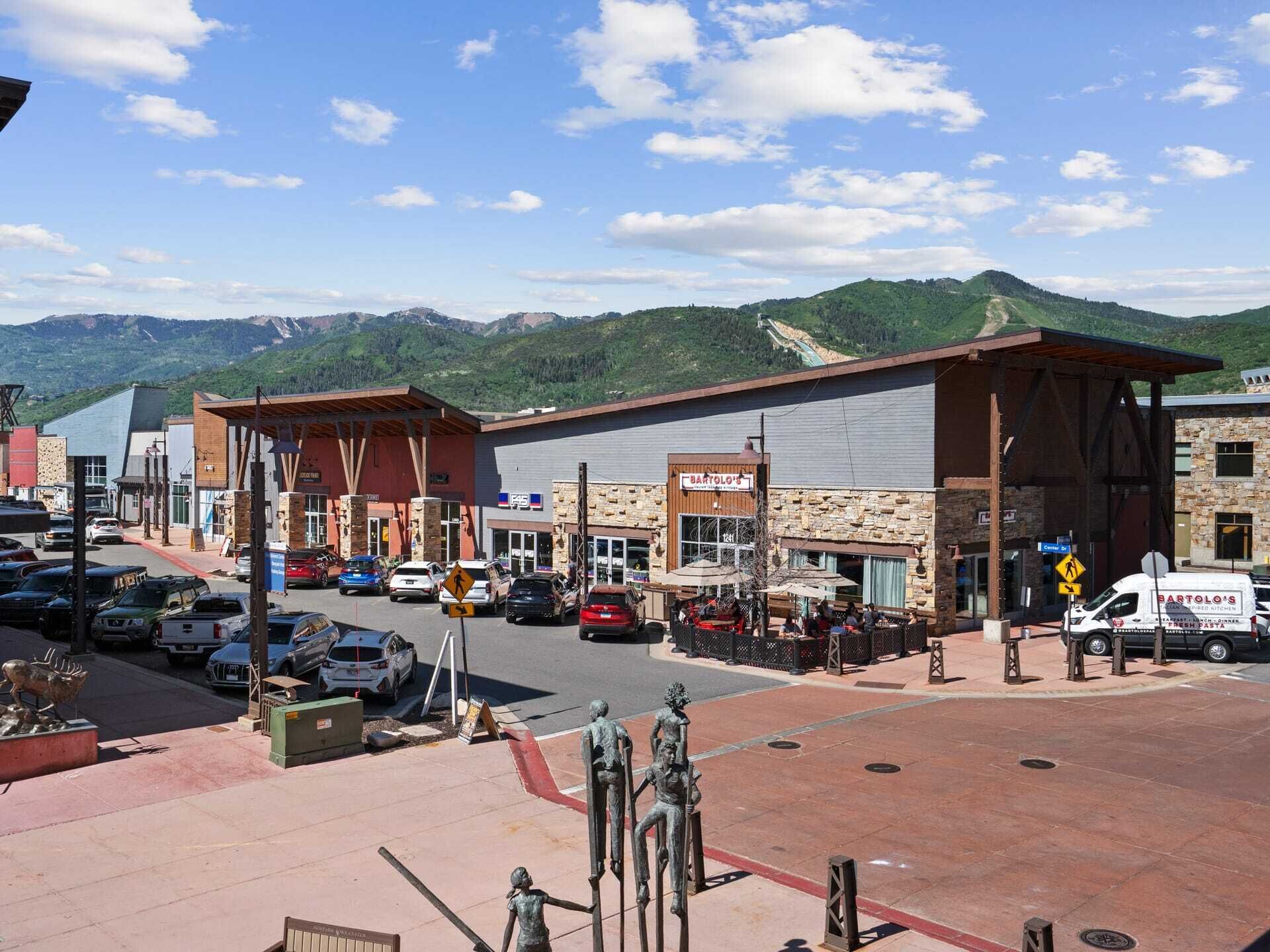 A town square with a Bartolo's restaurant, a parking lot, and a statue of a man holding a child.