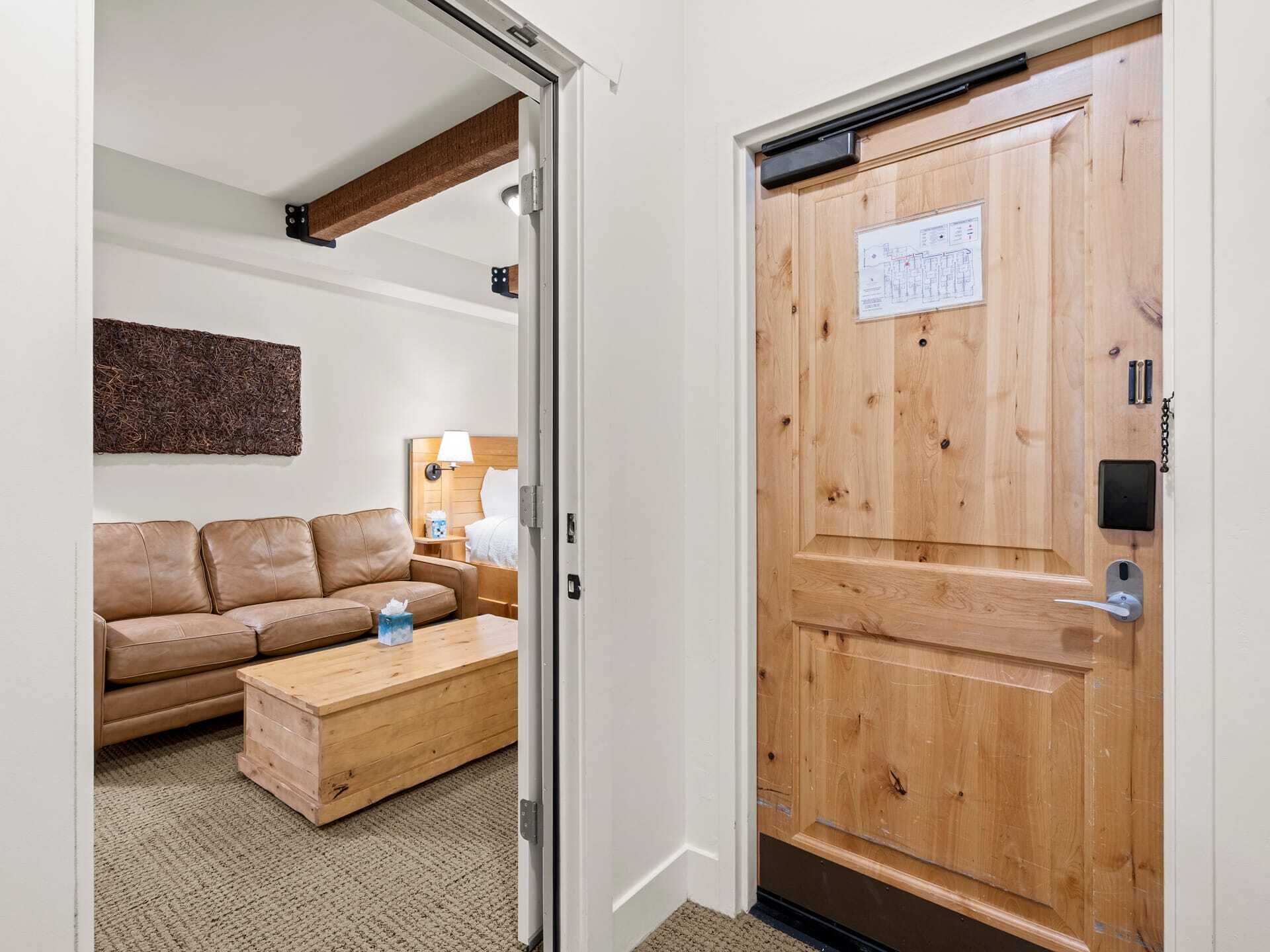 A room with a wooden door, a brown leather sofa, a wooden coffee table, and a lamp.