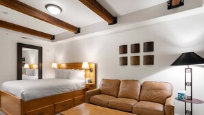 Ein Hotelzimmer mit einem großen Bett, einem Holztisch, einer Ledersofa und einem kleinen Beistelltisch.