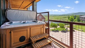 Ein Whirlpool auf einer Holzdielen-Terrasse mit Blick auf eine grüne Landschaft und ein rotes Gebäude in der Ferne.