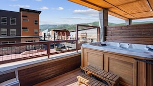 Una terraza de madera con un jacuzzi y escalones que conducen a un balcón con vistas a un pueblo.