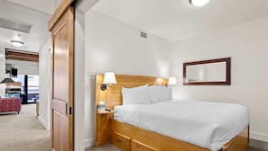 Habitación de hotel con cama de madera, lámparas de noche, televisor de pantalla plana y un espejo grande en la pared.
