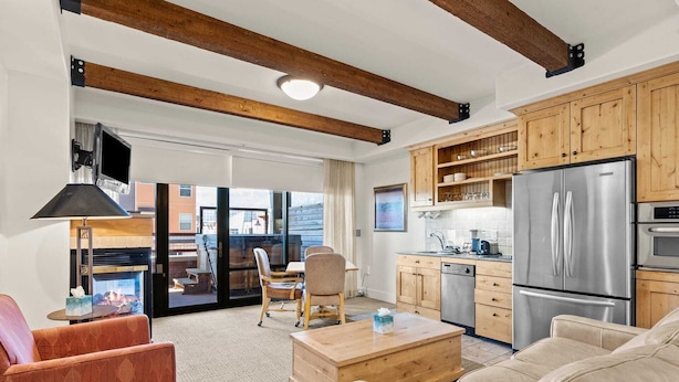 Una sala de estar moderna con chimenea, vigas de madera en el techo, una cocina con electrodomésticos de acero inoxidable y un amplio ventanal con vistas a la ciudad.